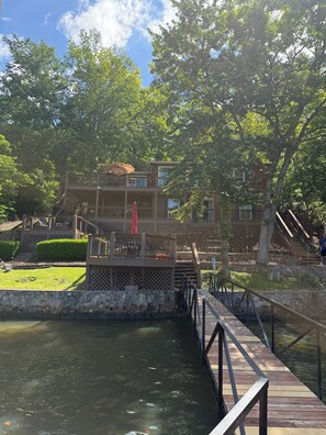 A wooden deck over a body of water, a multi-level building with outdoor seating, and a stone wall.