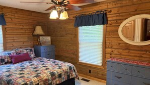 A bedroom with a bed, a dresser, a ceiling fan, a window with blinds, and a mirror. - Lakefront Rustic 4-Bedroom House with Private Dock (Lake Ozark)