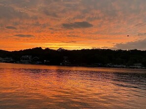 A sunset over a body of water with a silhouette of a hill and buildings in the background.