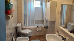 A bathroom with a toilet, bidet, bathtub, sink, and a towel rack with colorful towels.