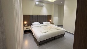 A modern hotel room with a large bed, a nightstand, a wall-mounted air conditioner, and recessed ceiling lighting. - 005 JRE Apartment With Stunning Boulevard Veiw (Amman)