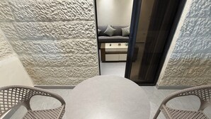 A round table with two wicker chairs in a room with textured walls and a view into another room with a sofa. - 005 JRE Apartment With Stunning Boulevard Veiw (Amman)