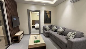 A modern living room with a grey sofa, a wooden coffee table, a TV, and a painting on the wall. - 005 JRE Apartment With Stunning Boulevard Veiw (Amman)
