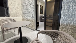 A modern room with a textured white wall, a round table with chairs, and a sliding glass door leading to a living area with a sofa and a painting. - 005 JRE Apartment With Stunning Boulevard Veiw (Amman)