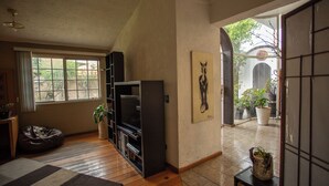 Een woonkamer met een houten vloer, een tv-meubel, een loungestoel en een groot raam.