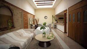 Een kamer met een bank, een ronde tafel met een plant, een dakvenster en houten deuren.