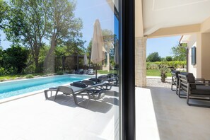 Ein Poolbereich mit Liegestühlen und Sonnenschirmen, freie Sicht auf den Pool sowie ein Garten mit Bäumen und einem Weinberg im Hintergrund.