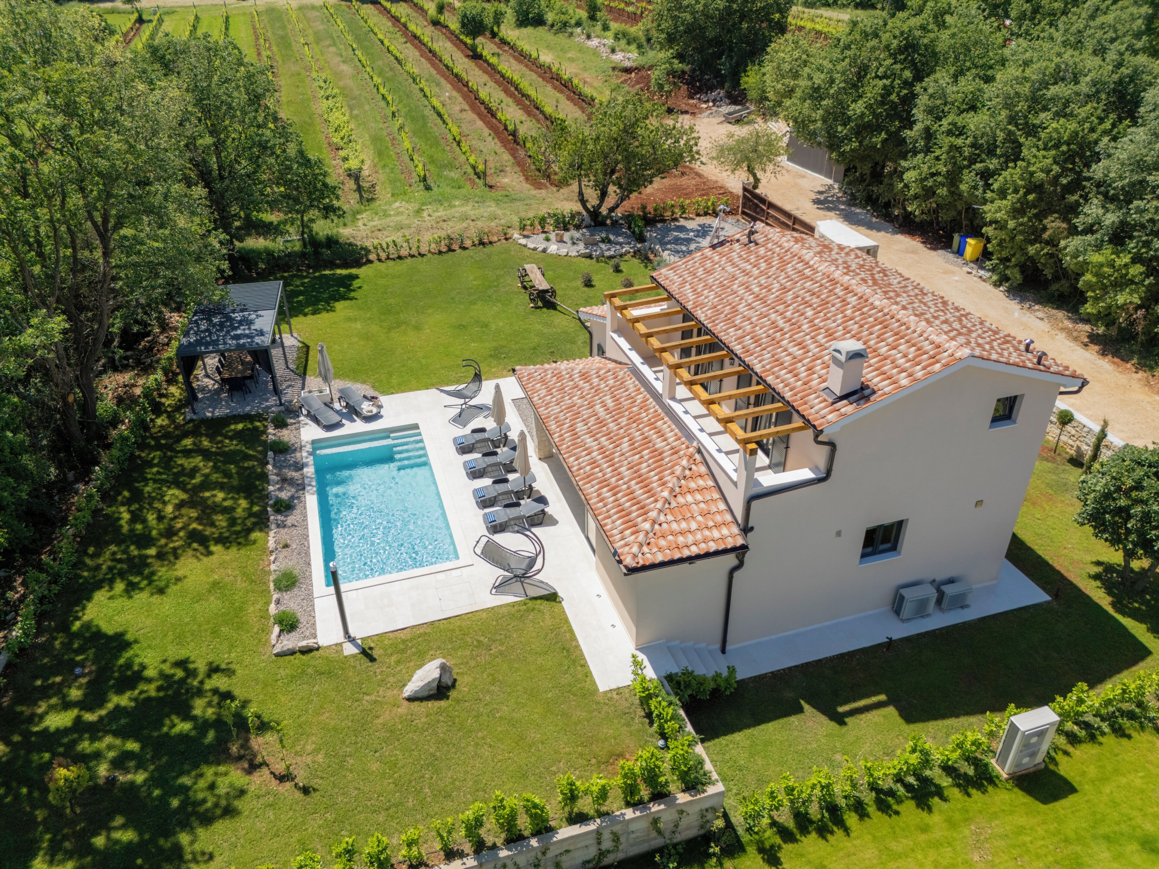 A two-story house with a swimming pool, outdoor seating, and a vineyard in the background.
