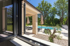 A poolside area with a covered patio, outdoor furniture, and a view of a swimming pool.