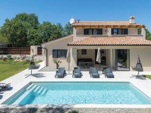 A two-story house with a swimming pool, outdoor seating, and a garden.