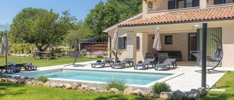 A two-story house with a swimming pool, outdoor seating, and a garden.