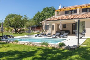 A two-story house with a swimming pool, outdoor seating, and a garden.