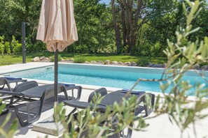 A swimming pool with lounge chairs and an umbrella, surrounded by greenery.