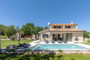 A two-story house with a swimming pool, outdoor seating, and a garden.