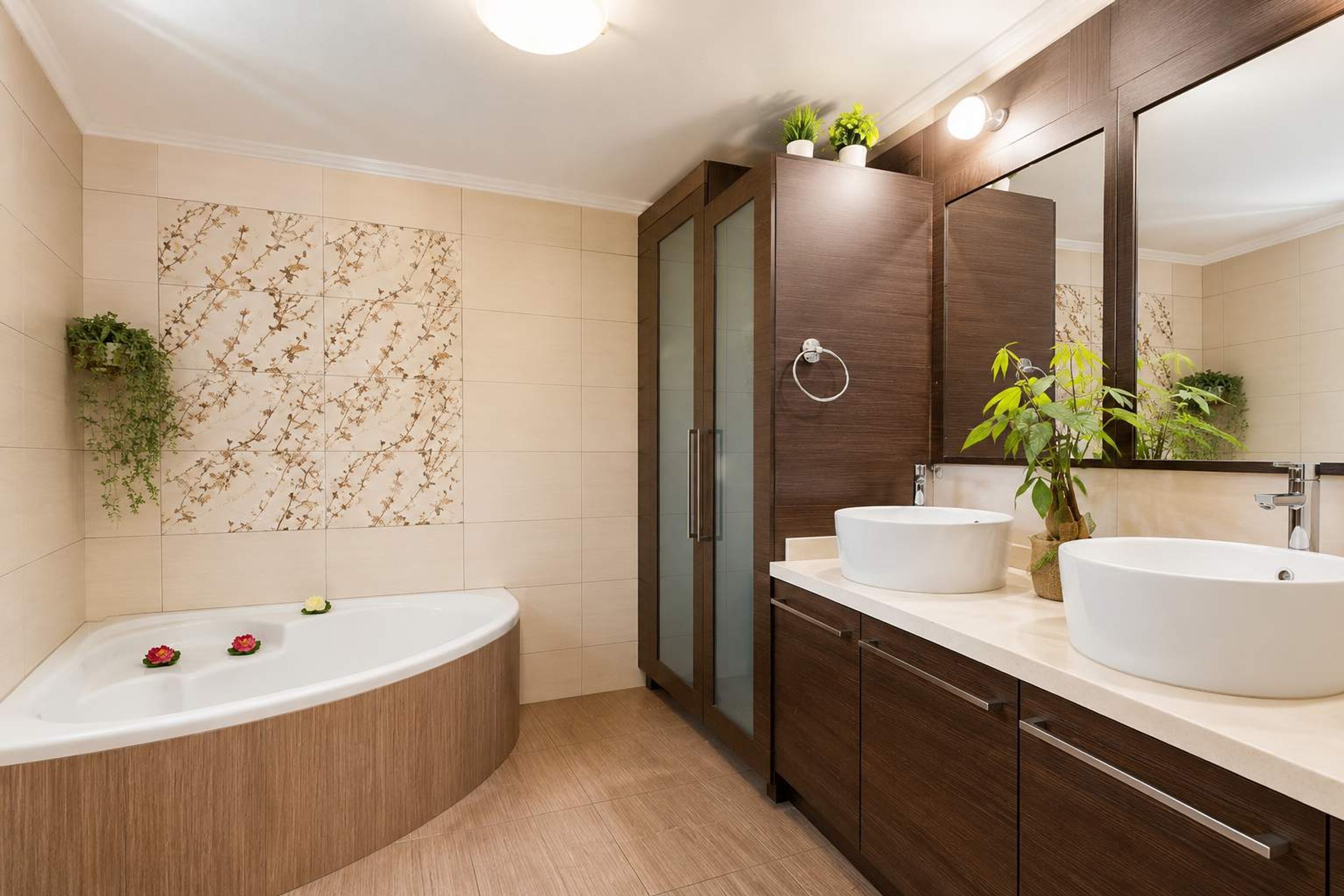A modern bathroom with a freestanding bathtub, two sinks, a large mirror, and decorative plants.