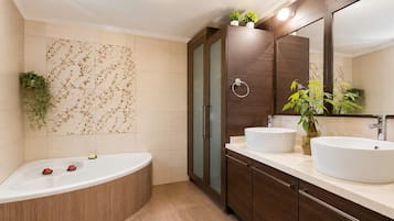 A modern bathroom with a freestanding bathtub, two sinks, a large mirror, and decorative plants.