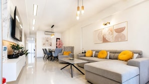 A modern living room with a grey sofa, a coffee table, and a dining area with chairs and a table. - Fems Luxury 3-level Home w Private Jacuzzi (Heraklion)