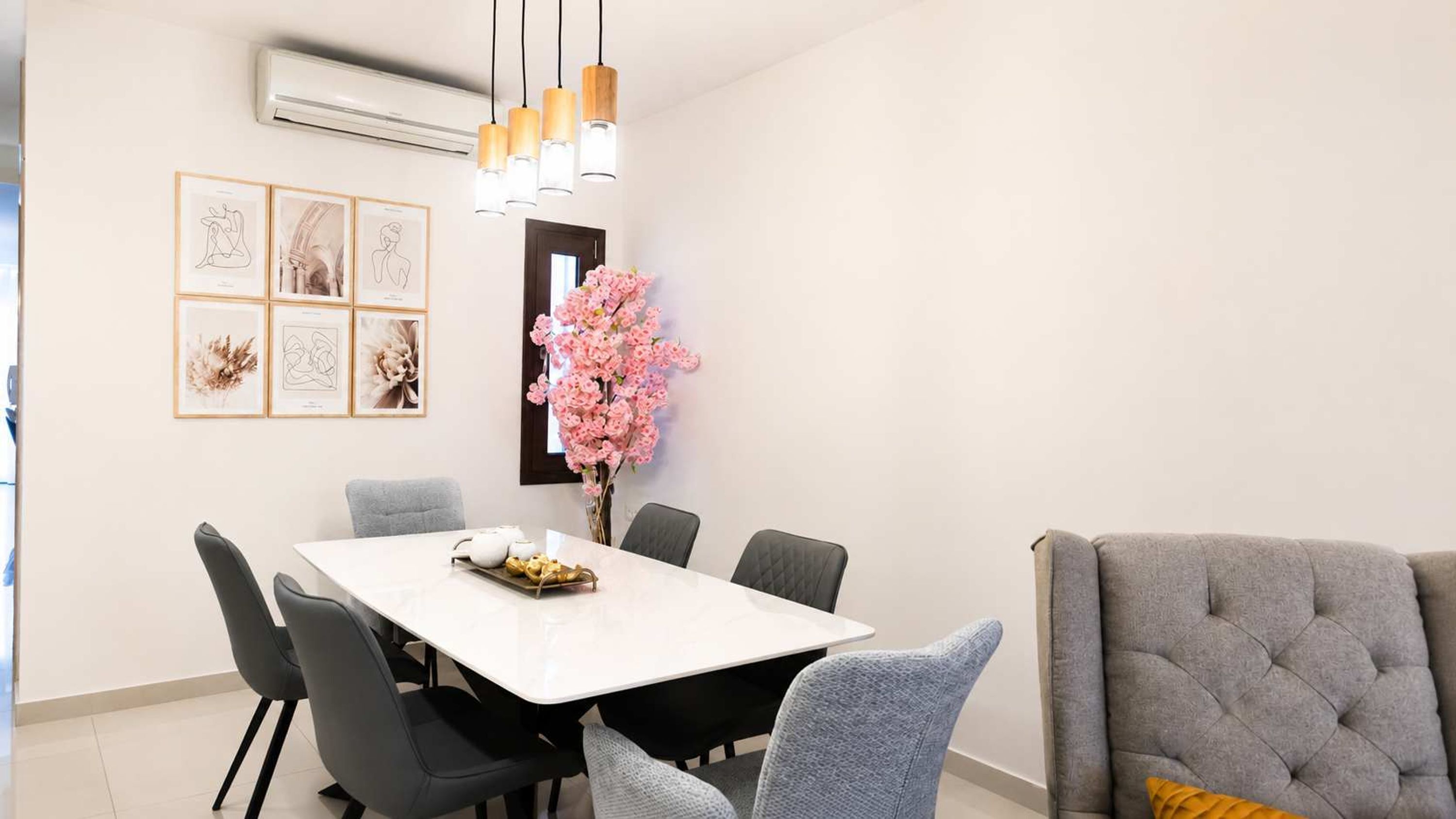 Een eetruimte met een witte tafel, zwarte stoelen, een vaas met roze bloemen en lijstwerken aan de muur.