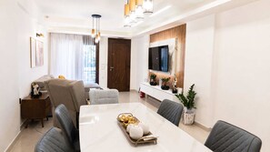 A modern dining area with a long table, multiple chairs, a TV mounted on the wall, and a wooden door. - Fems Luxury 3-level Home w Private Jacuzzi (Heraklion)