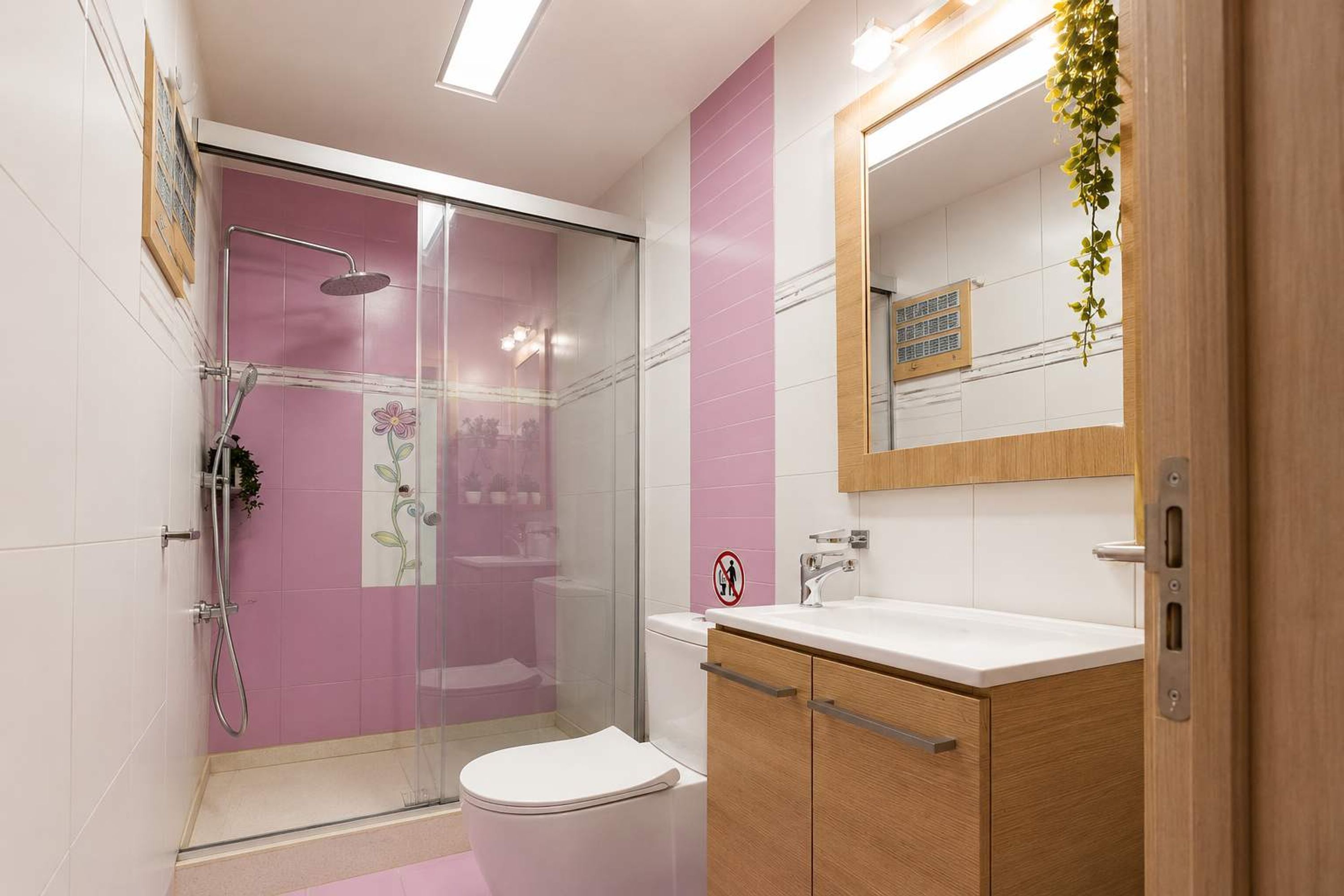 Een moderne badkamer met een douchecabine van glas, een toilet, een wastafel met spiegel en houten kastjes.