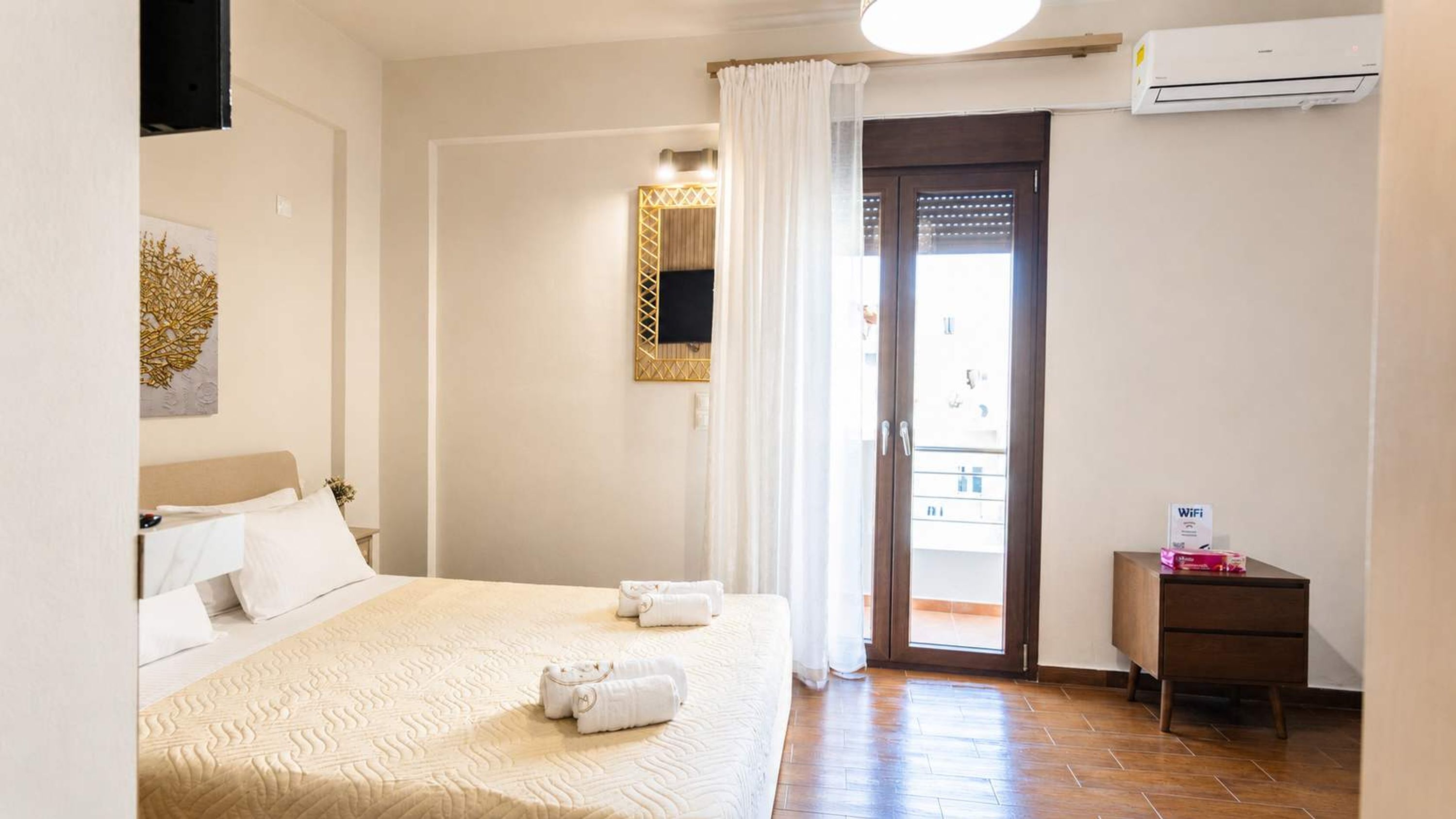A hotel room with a bed, a bedside table, a mirror, a door leading to a balcony, and an air conditioning unit.