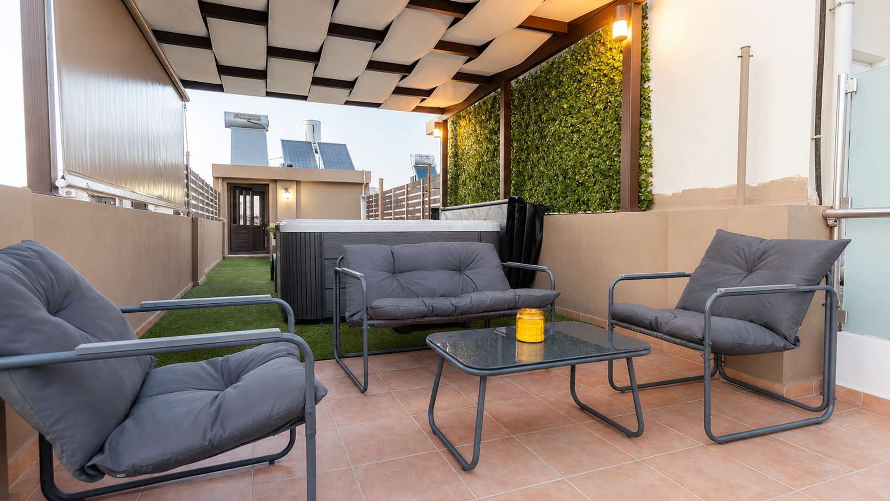 A patio with a sofa, chairs, and a table, a hot tub, and a green wall with plants.