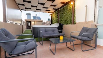 A patio with a sofa, chairs, and a table, a hot tub, and a green wall with plants.