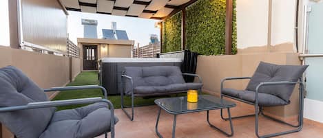 Eine Terrasse mit einer Couch, Stühlen, einem Tisch, einem Whirlpool und einer grünen Wand mit Pflanzen.