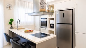 A modern kitchen with a stainless steel refrigerator, a built-in oven, a glass shelf, and a small island with a sink and a fruit basket. - Fems Luxury 3-level Home w Private Jacuzzi (Heraklion)