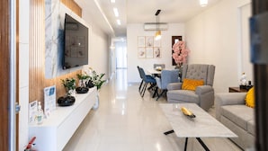A modern living room with a flat-screen TV, a dining area with chairs, a grey armchair, and a coffee table. - Fems Luxury 3-level Home w Private Jacuzzi (Heraklion)