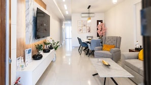 A modern living room with a flat-screen TV, a dining area with chairs, a grey armchair, and a coffee table. - Fems Luxury 3-level Home w Private Jacuzzi (Heraklion)