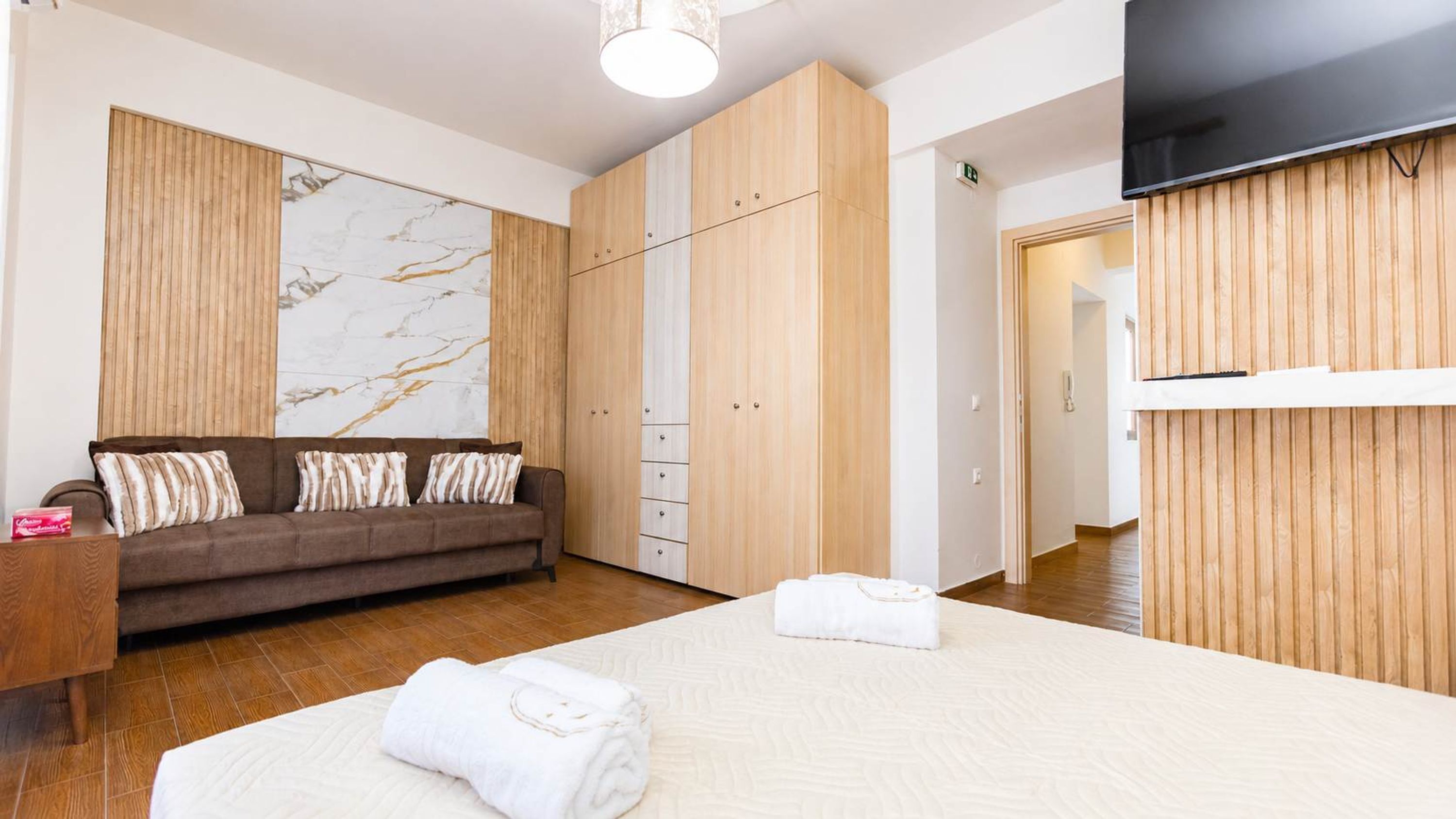 Et hotelværelse med en seng, sofa, træskab og fjernsyn.