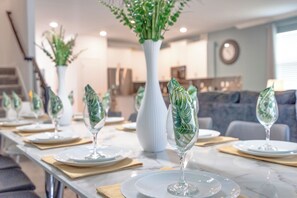 A dining area with a long table set for a meal, featuring clear glassware and a central white vase with green foliage. - Game Room/SPA/Themed Bedrooms/Storey Lake 22088 (Kissimmee)
