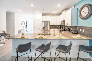 A modern kitchen with a central island, bar stools, and a large wall clock. - Game Room/SPA/Themed Bedrooms/Storey Lake 22088 (Kissimmee)