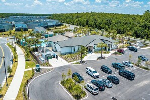 A large parking lot with multiple cars, a building with a grey roof, and a green landscape in the background. - Game Room/SPA/Themed Bedrooms/Storey Lake 22088 (Kissimmee)