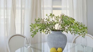 En matplats med ett glasbord, vita stolar, en vas med gröna blad och en skål med citroner.