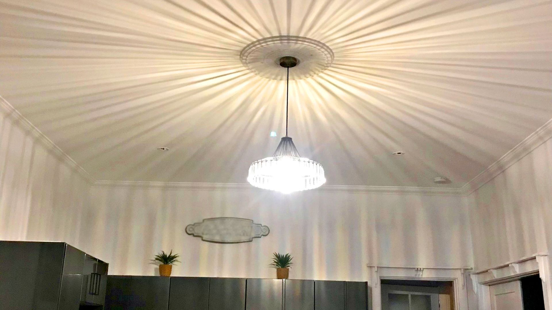 A room with a high ceiling, a chandelier, and two potted plants.