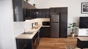 Una cocina moderna con armarios negros, un refrigerador de acero inoxidable, un microondas y un lavamanos.