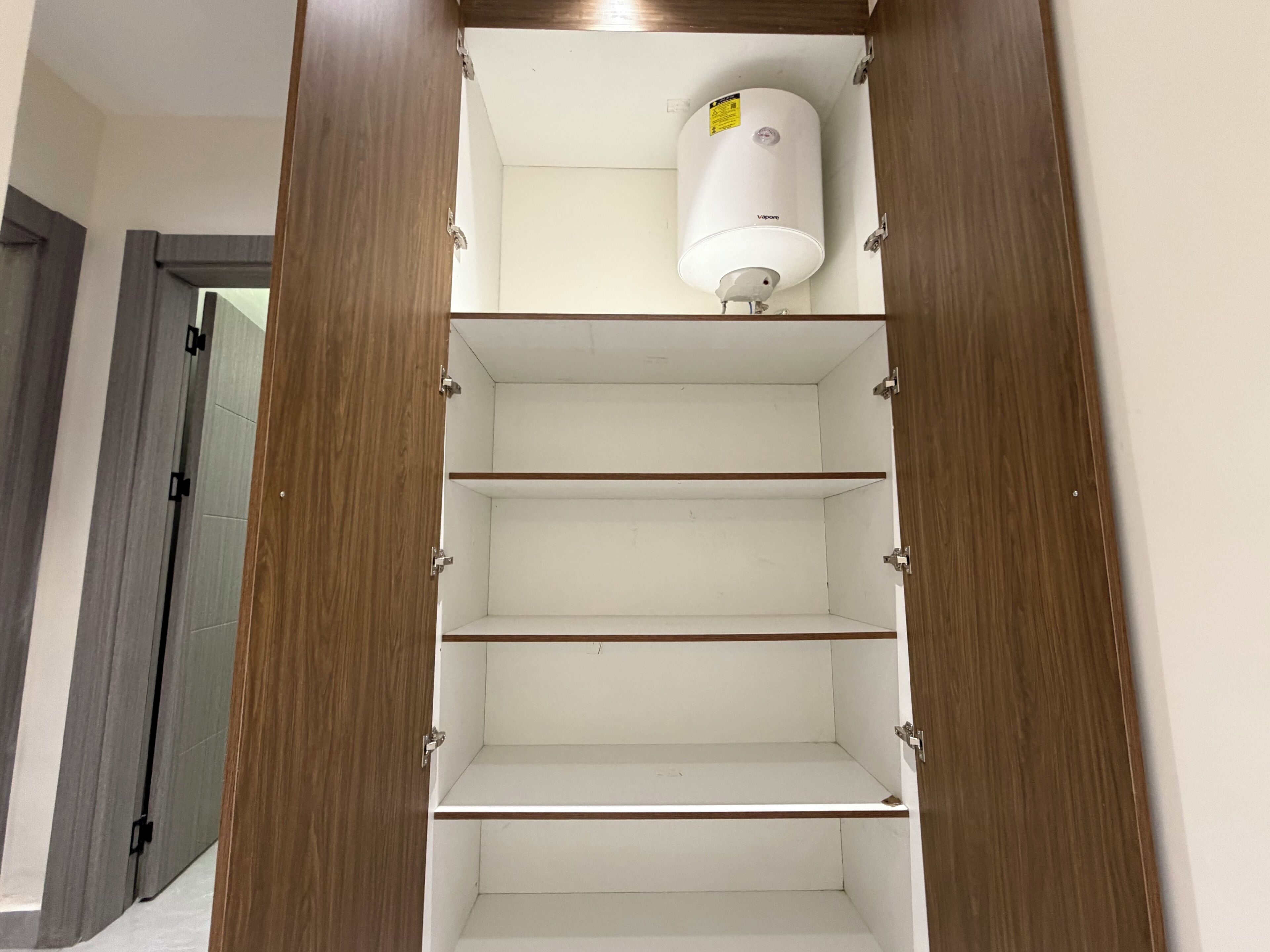 Un armario con puertas de madera y tres repisas, una de las cuales tiene un objeto cilíndrico blanco encima.