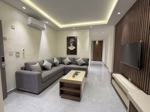 Un salon moderne avec un canapé d’angle, une table basse, un téléviseur à écran plat et un mur décoratif en bois.