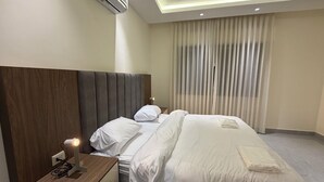 Une chambre d’hôtel avec un grand lit, une table de chevet avec une lampe, un climatiseur et une fenêtre avec des rideaux.