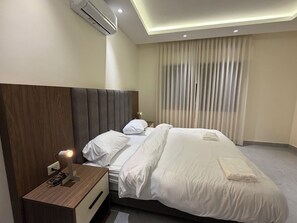 Une chambre d’hôtel avec un grand lit, une table de chevet avec une lampe, un climatiseur et une fenêtre avec des rideaux.