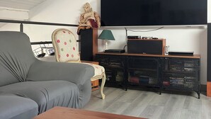 A modern living room with a grey sofa, a wooden coffee table, a TV mounted on the wall, a lamp, and a small statue. - Friendly house surrounded by greenery. (Biriatou)