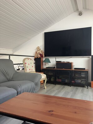 A modern living room with a grey sofa, a wooden coffee table, a TV mounted on the wall, a lamp, and a small statue. - Friendly house surrounded by greenery. (Biriatou)