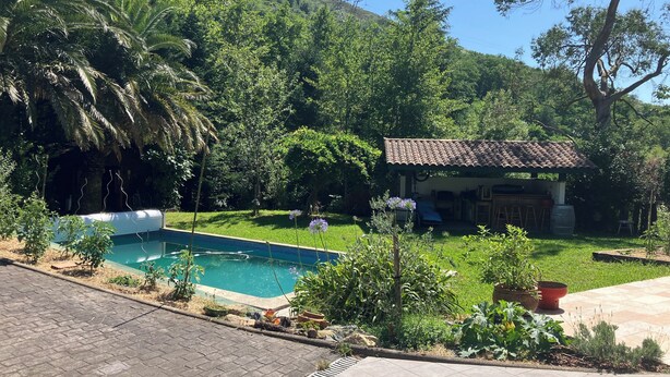 A swimming pool, a small house with a tiled roof, and lush greenery. - Friendly house surrounded by greenery. (Biriatou)