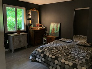 A bedroom with a bed, dresser, vanity, and a window with a view of greenery. - Friendly house surrounded by greenery. (Biriatou)