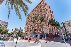 Ein mehrstöckiges Hotel mit Balkonen, Palmen und Blick auf die Straße.