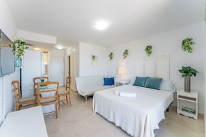 Ein Hotelzimmer mit einem Bett, einem kleinen Tisch mit Stühlen, einem Sofa, einem Nachttisch mit Lampe und Wandpflanzen.