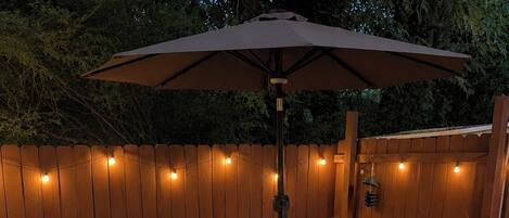 An outdoor patio with a checkered floor, a wooden table, chairs, and an umbrella.