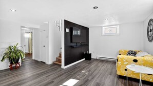 A modern living room with a sofa, a TV, and a staircase leading to another room.